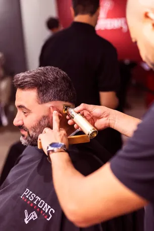 Acabamento da barba com máquina dourada, cliente com a capa Pistons