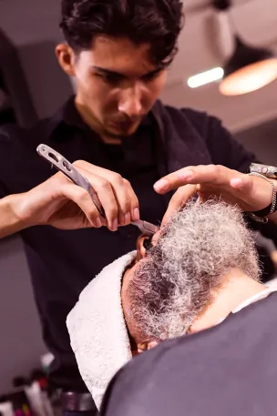 Barbeiro concentrado desenhando a barba com navalha e toalha quente